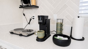 A kitchen with a coffee maker, a scale, a mug, a bowl with tea bags, and a paper towel holder.