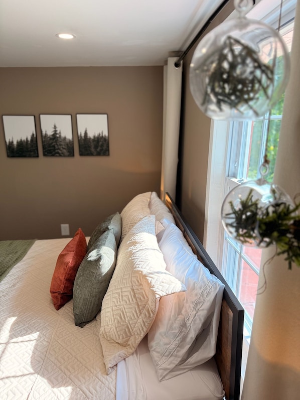 A bedroom with a bed, pillows, a window with a view, and wall art.