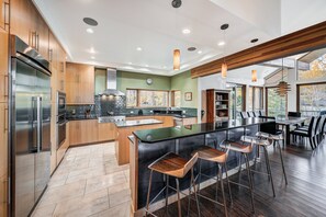 A modern kitchen with a central island, bar stools, and a dining area with a view. - NEW Cloud 9 Cabin in Warrior's Mark near Peak 9 & 10. Amazing Views & Mtn Access! (Breckenridge)