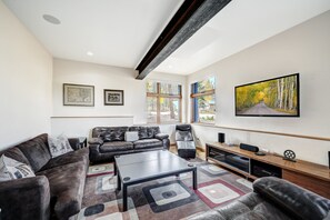 A modern living room with a sofa, armchair, and a coffee table. There are framed pictures on the wall and a large TV mounted above the coffee table. - NEW Cloud 9 Cabin in Warrior's Mark near Peak 9 & 10. Amazing Views & Mtn Access! (Breckenridge)