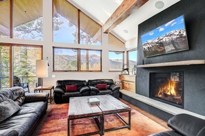 A spacious living room with a fireplace, leather sofas, a coffee table, and large windows offering mountain views. - NEW Cloud 9 Cabin in Warrior's Mark near Peak 9 & 10. Amazing Views & Mtn Access! (Breckenridge)
