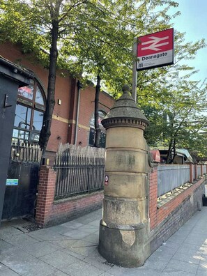 A street sign for Deansgate station with a metal pillar and a brick wall in the background. - 2BR Manchester Apartment near Old Trafford (Manchester)