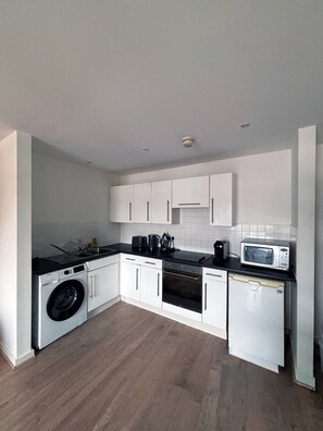 A modern kitchen with white cabinetry, a built-in washing machine, a microwave, and a dishwasher. - 2BR Manchester Apartment near Old Trafford (Manchester)