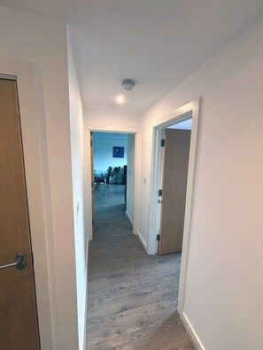 A narrow hallway with wooden flooring leading to a room with a bed and a window. - 2BR Manchester Apartment near Old Trafford (Manchester)