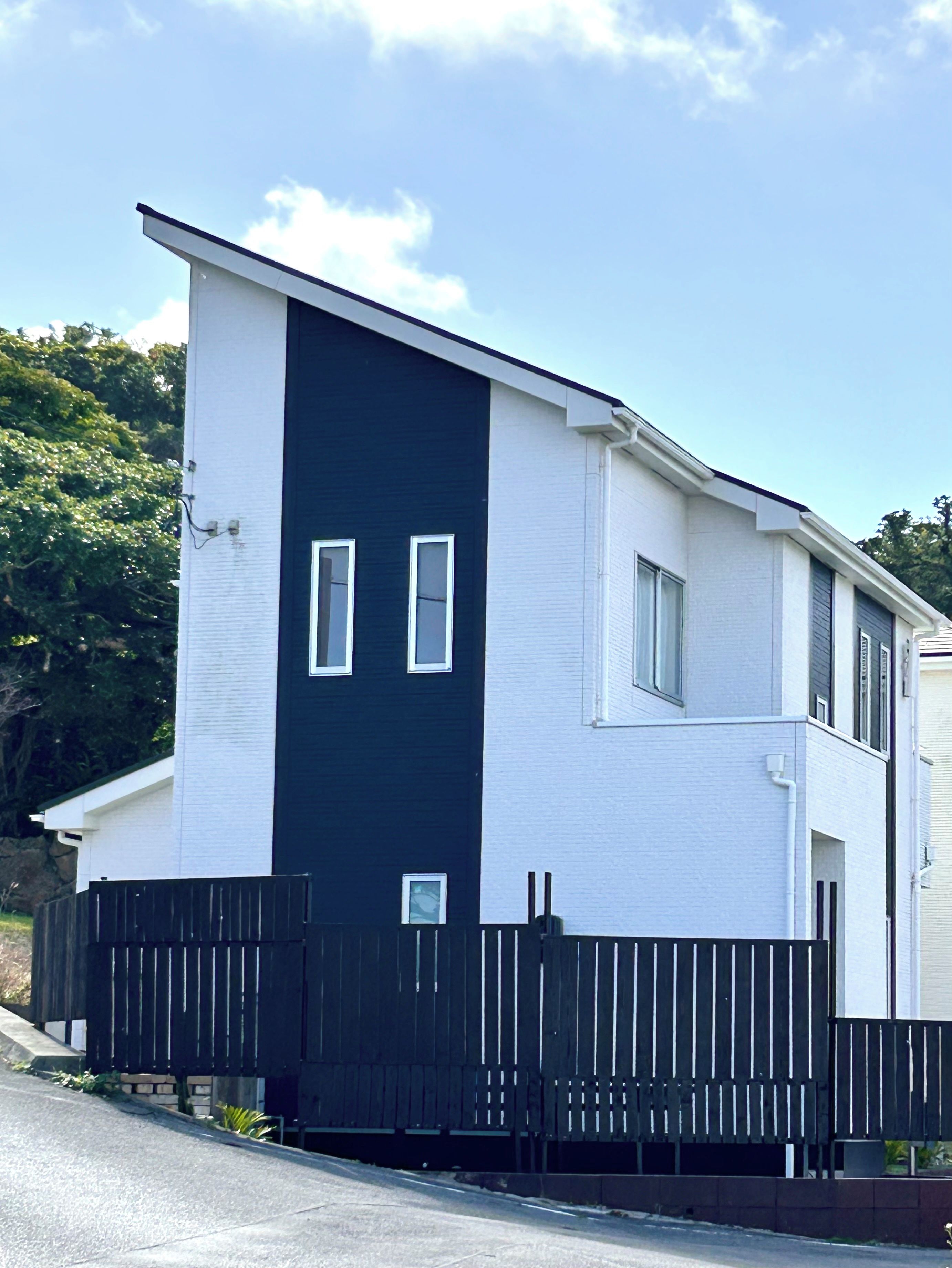 A modern two-story building with a white facade and a black vertical section, a black fence, and a clear sky.