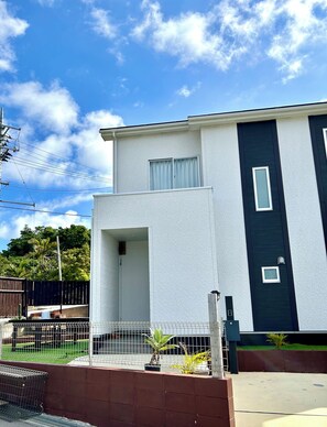 A modern two-story building with a white exterior and dark accents, a fenced yard, and a clear sky.
