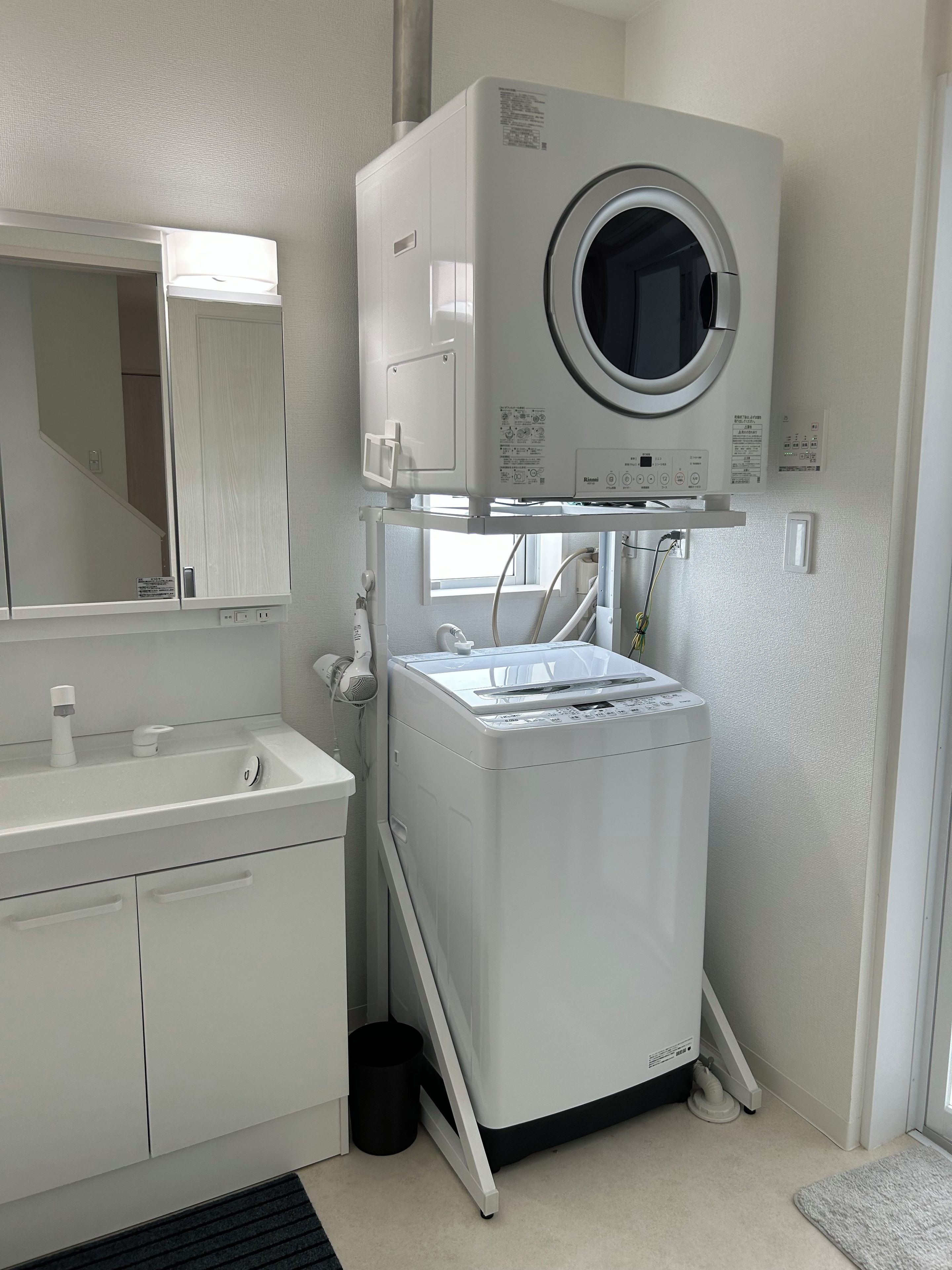 A compact, modern bathroom with a built-in washer and dryer, a sink with a mirror, and a small trash bin.