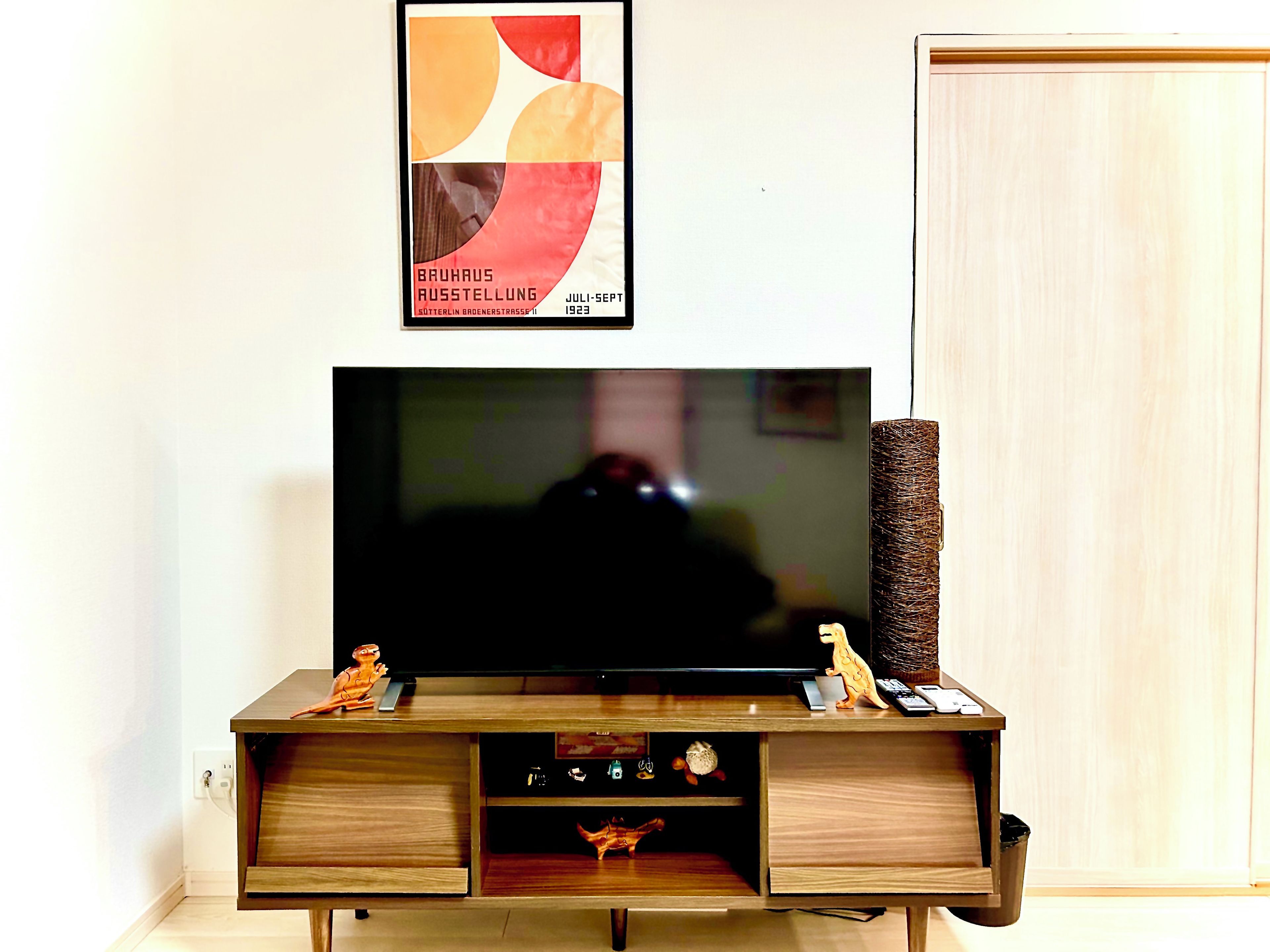 A flat-screen TV mounted on a wooden TV stand with a poster above it.