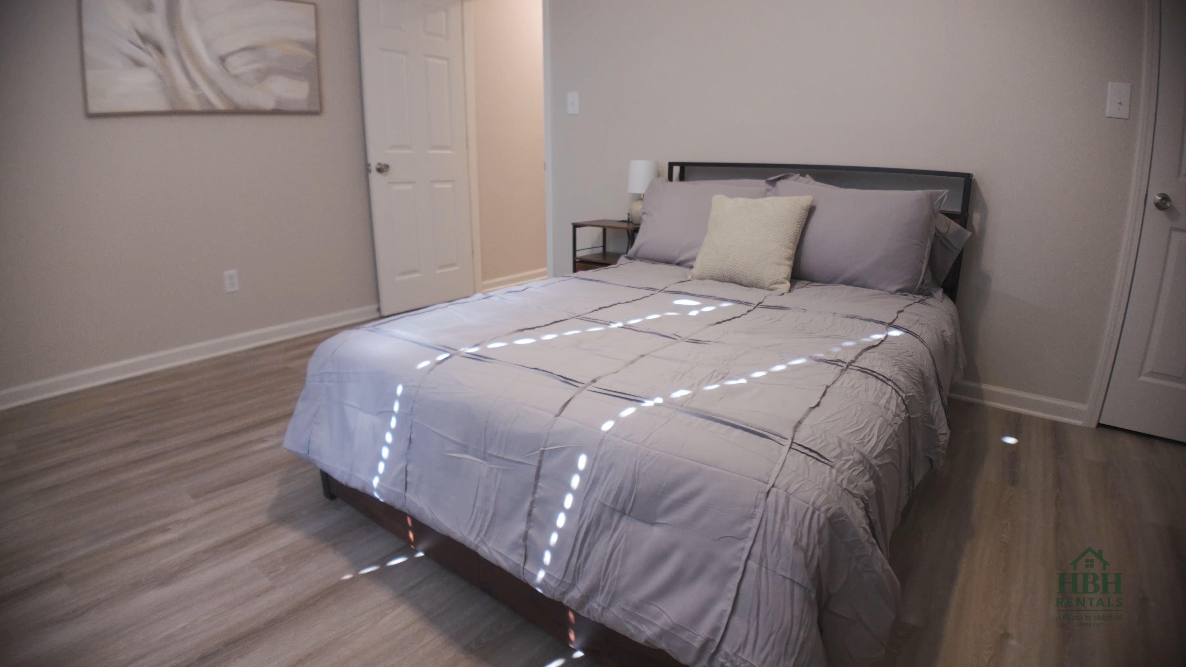 Un dormitorio con una cama, una mesita de noche, una lámpara y una puerta.