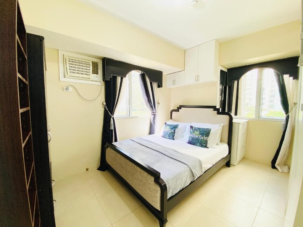 A bedroom with a bed, a window with curtains, a bedside table, and a wall-mounted air conditioning unit.