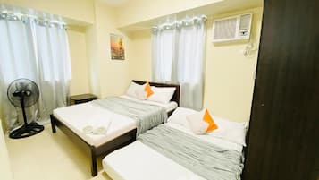 Ein Zimmer mit zwei Betten, einem Standventilator und einer Tür.