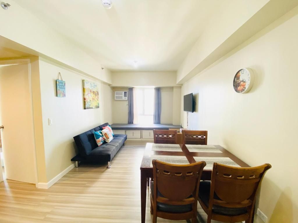 A dining area with a table and chairs, a sofa, and a television on the wall.