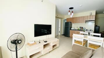 Ein modernes Wohnzimmer mit Flachbildfernseher, Standventilator, Sofa und Essbereich mit weißem Tisch und Stühlen.