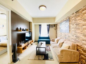 A modern living room with a sofa, coffee table, TV, and a stone-patterned wall. - Cebu Avida Riala Towers by P&J (Cebu City)