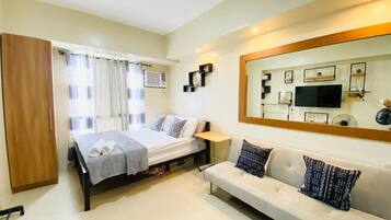 Un dormitorio con cama, sofá, armario, espejo y televisión.