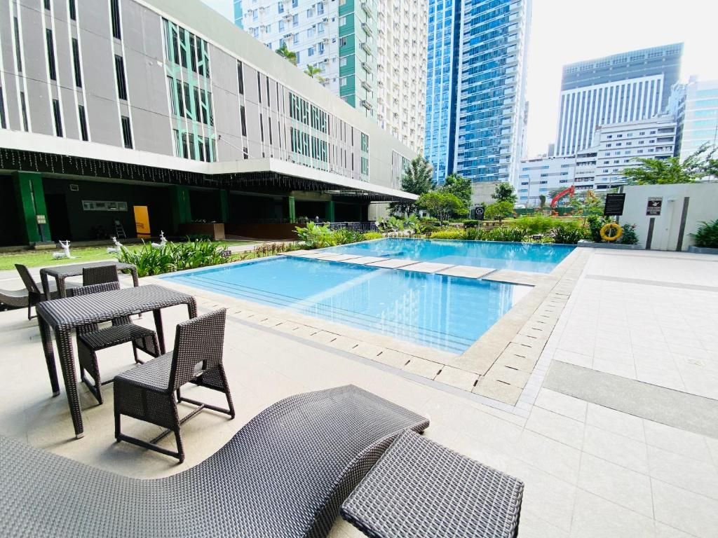 A rooftop pool area with lounge chairs and a dining table, surrounded by modern buildings.