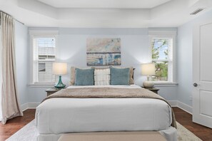 Quarto com uma cama grande, duas mesas de cabeceira com abajures, um quadro na parede e janelas com persianas.