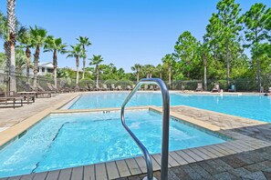 Piscina com escada de metal, cercada por cadeiras de descanso e palmeiras.