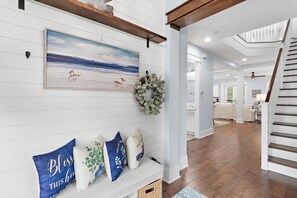 A hallway with a bench, a painting, and a wreath. - Maison de Paix | Luxury NatureWalk Home | Golf Cart + 6 Bikes | Sleeps 11 (Santa Rosa Beach)