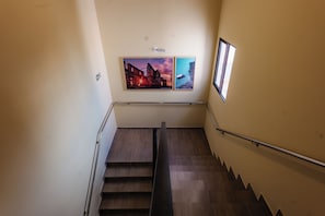 A staircase with a handrail, a wall-mounted emergency exit sign, and two framed pictures.