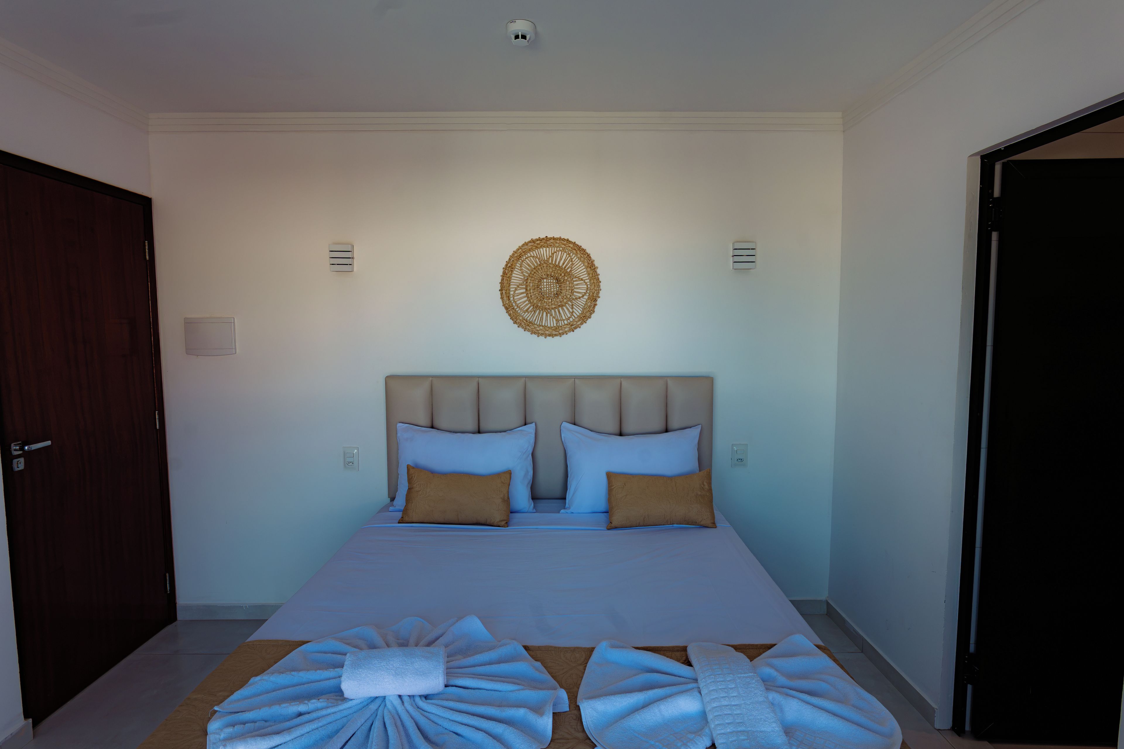 Een slaapkamer met een bed, twee nachtkastjes, een decoratief object aan de muur en een deur.