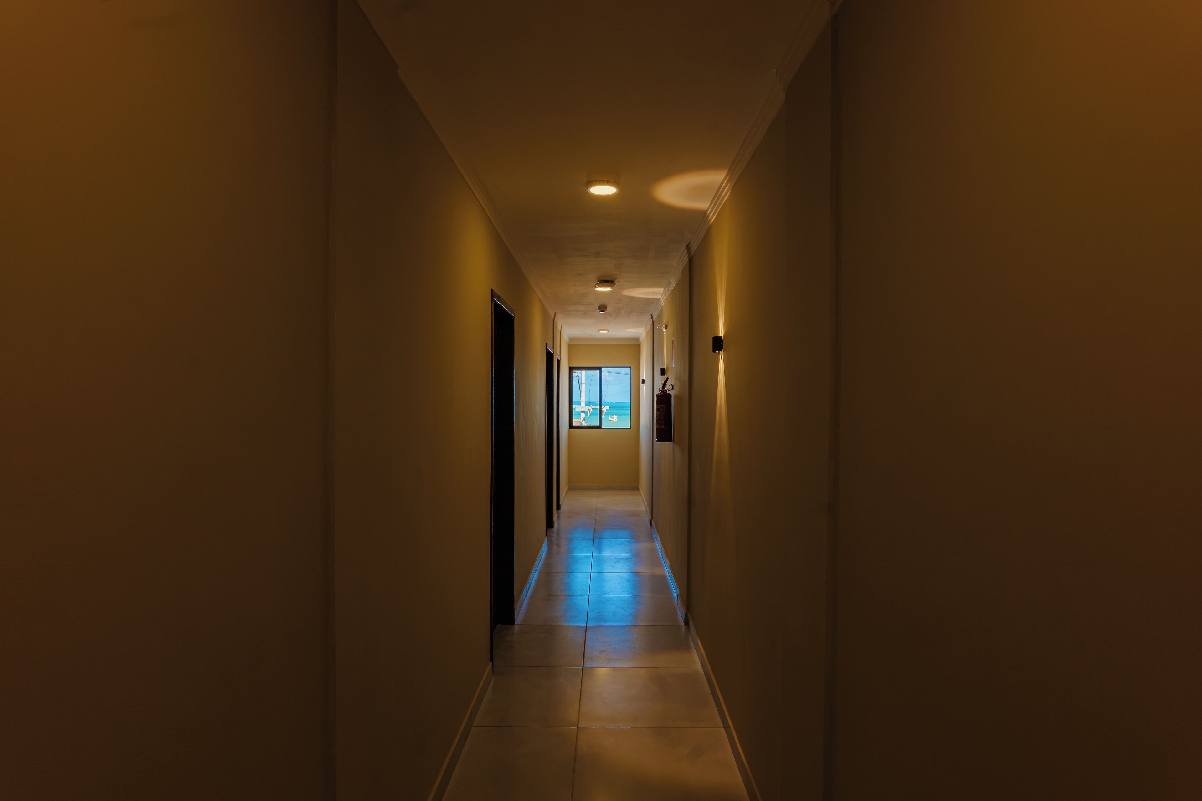 A narrow, well-lit hallway with a tiled floor, leading to a door at the end.