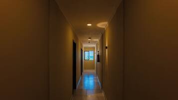 A narrow, well-lit hallway with a tiled floor, leading to a door at the end.