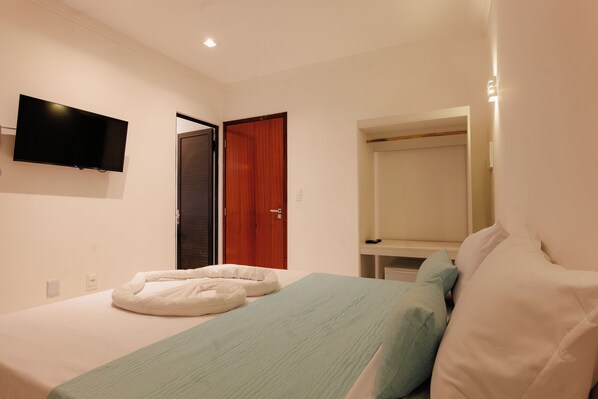 Un dormitorio con una cama, un televisor montado en la pared y una puerta de madera.