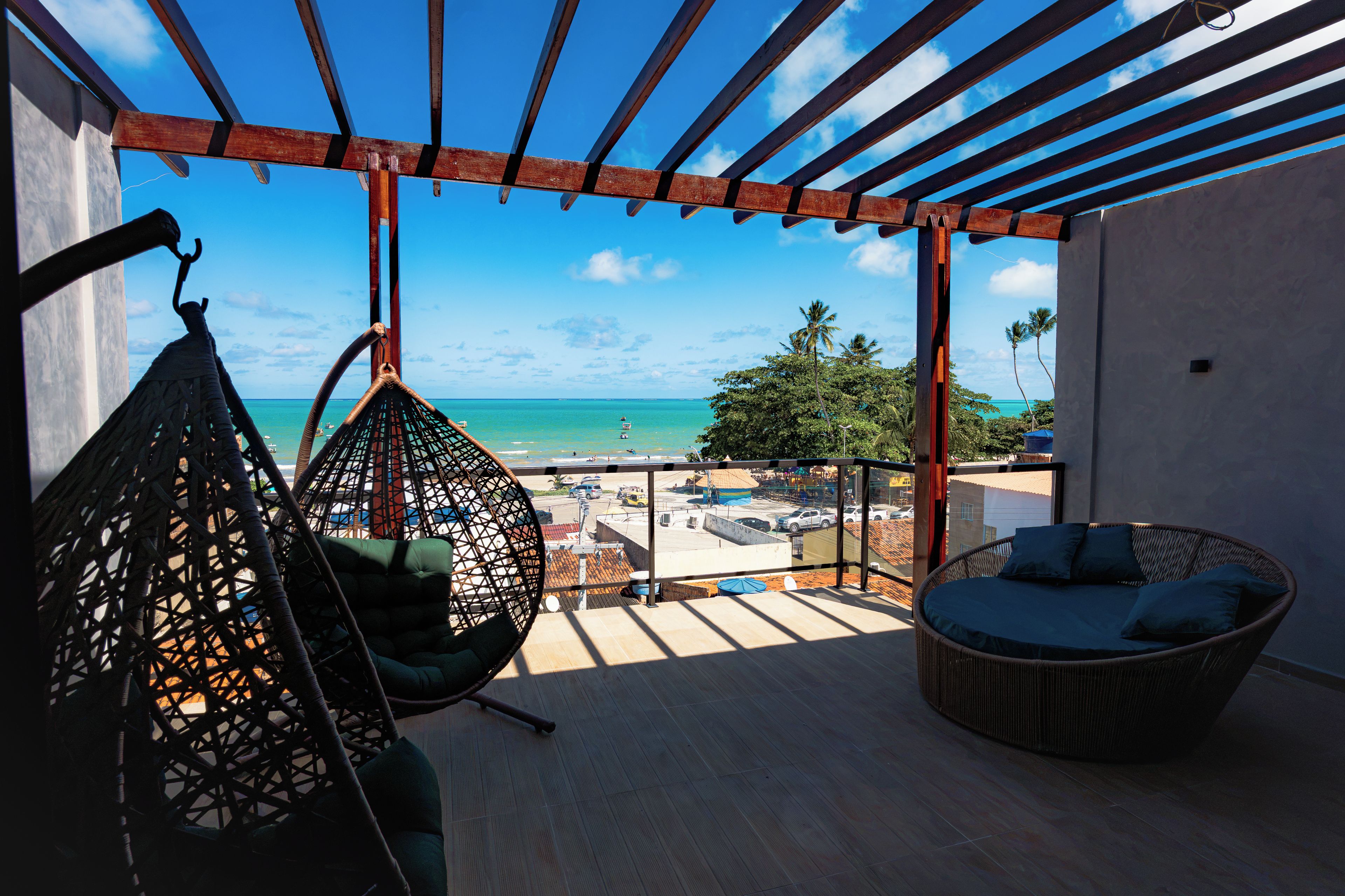 A balcony with a view of the ocean, a hanging chair, a wicker sofa, and a wooden floor.