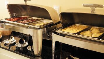 A buffet setup with various food items in metal serving trays, a spoon on a plate, and a black countertop.