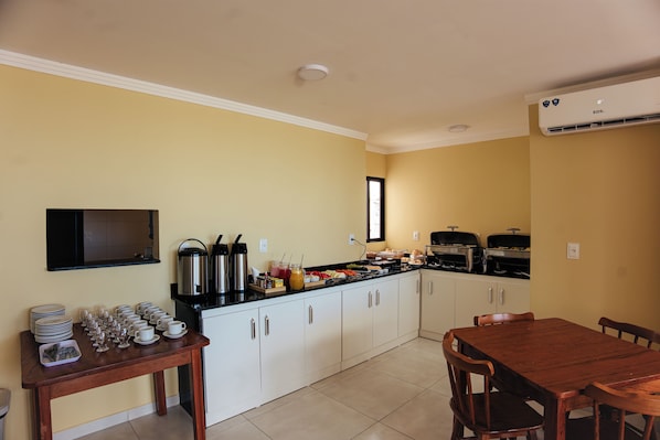 A kitchen with a dining table and chairs, a coffee station, and a TV mounted on the wall.