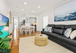 Un salon moderne avec un canapé en cuir noir, une table basse en verre et un coin repas avec des chaises blanches.