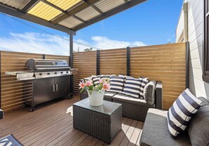 An outdoor patio with a grill, wicker furniture, and a potted plant. - Salty Air Coastal Cottage, Pet Friendly (Lake Illawarra)