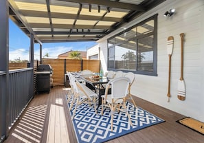 Un patio couvert avec une table et des chaises, un barbecue et une vue sur le quartier.
