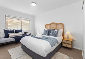 Une chambre à coucher avec un lit, des tables de chevet, une lampe et une fenêtre avec des stores.