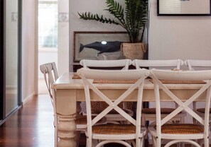A dining area with a white table and chairs, a woven placemat, and a framed picture of a fish on the wall. - Salty Air Coastal Cottage, Pet Friendly (Lake Illawarra)