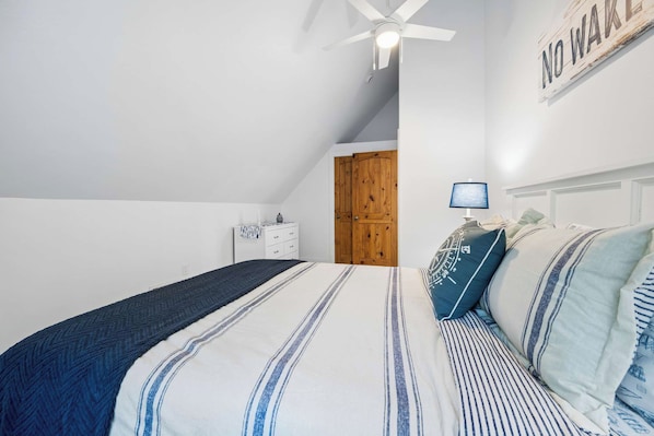 Un dormitorio con cama, mesita de noche, ventilador de techo y una puerta.