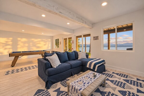 A cozy living room with a pool table, a sectional sofa, and a view of a lake.
