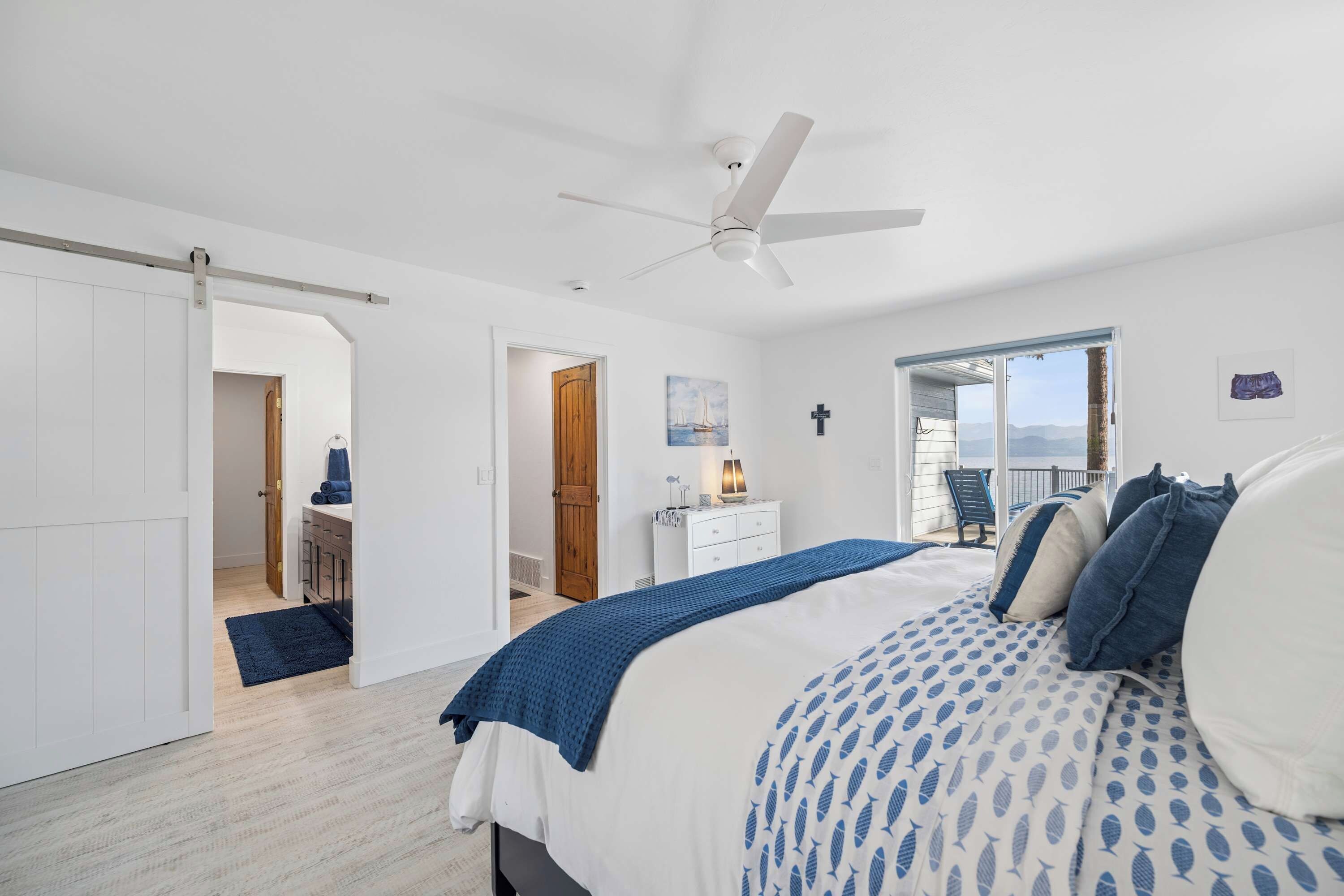 A bedroom with a bed, a ceiling fan, a dresser, and a view of the outdoors.