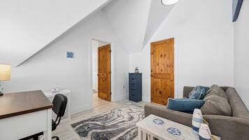 A loft-style room with a desk, chair, sofa, and a small table with decorative items.