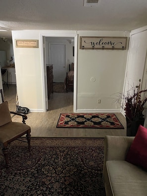 A living room with a sofa, a chair, a rug, a welcome sign, and a door leading to another room. - Cozy and Comfy "Away from Home" (Pine Bluff)