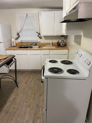 A compact kitchen with a white stove, a sink, and a window with curtains. - Cozy and Comfy "Away from Home" (Pine Bluff)