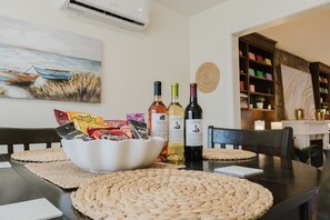 A dining table with a woven placemat, a bowl of snacks, and two bottles of wine. - LUX Heaven Sydney | 5BR, Pool Table, BBQ & Fireplace (Sydney)