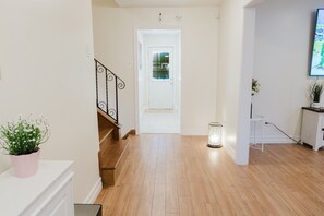 A hallway with a wooden staircase, a white door, a small table with a plant, and a floor lamp. - LUX Heaven Sydney | 5BR, Pool Table, BBQ & Fireplace (Sydney)