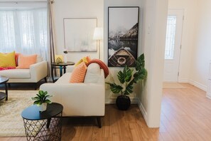 A living room with a white sofa, a small round table, and a potted plant. - LUX Heaven Sydney | 5BR, Pool Table, BBQ & Fireplace (Sydney)