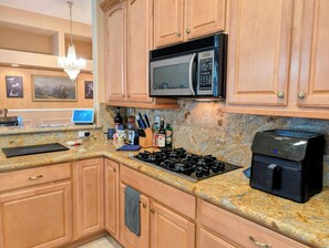 A kitchen with wooden cabinets, a granite countertop, a microwave, a stove, and a coffee maker. - Poolside Retreat in North Summerlin (Las Vegas)