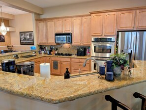 A modern kitchen with granite countertops, stainless steel appliances, and wooden cabinets. - Poolside Retreat in North Summerlin (Las Vegas)