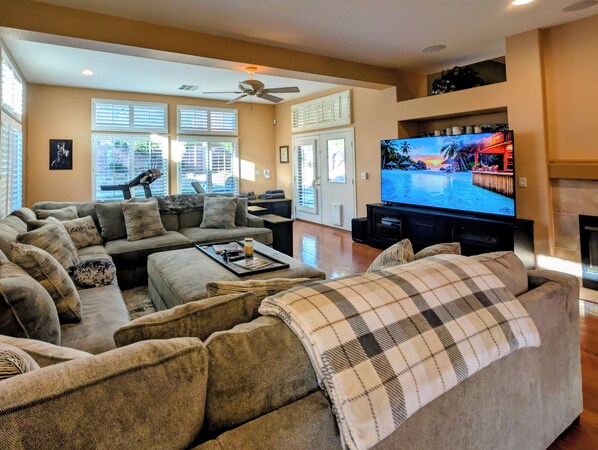 A living room with a large flat-screen TV, a sofa, a coffee table, and a fireplace. - Poolside Retreat in North Summerlin (Las Vegas)