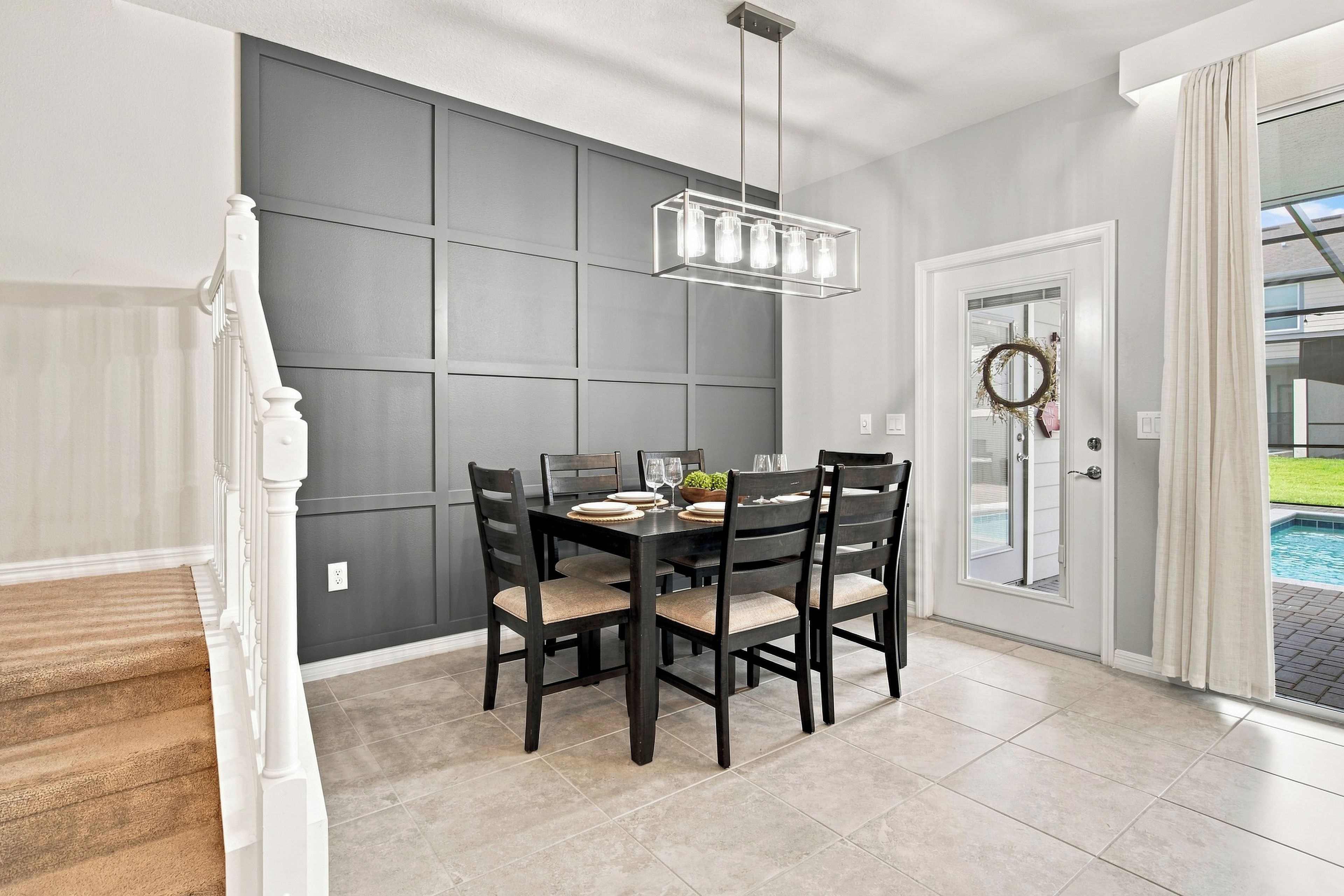 A dining area with a dark wooden table set for four, a modern pendant light, and a view of a swimming pool through a glass door.
