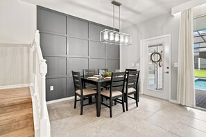 A dining area with a dark wooden table set for four, a modern pendant light, and a view of a swimming pool through a glass door. - Super Mario, Avengers & Harry Potter Rooms (Davenport)